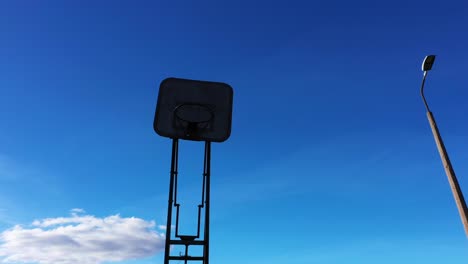 silhouette of old basketball hoop against blue sky, low angle orbit view