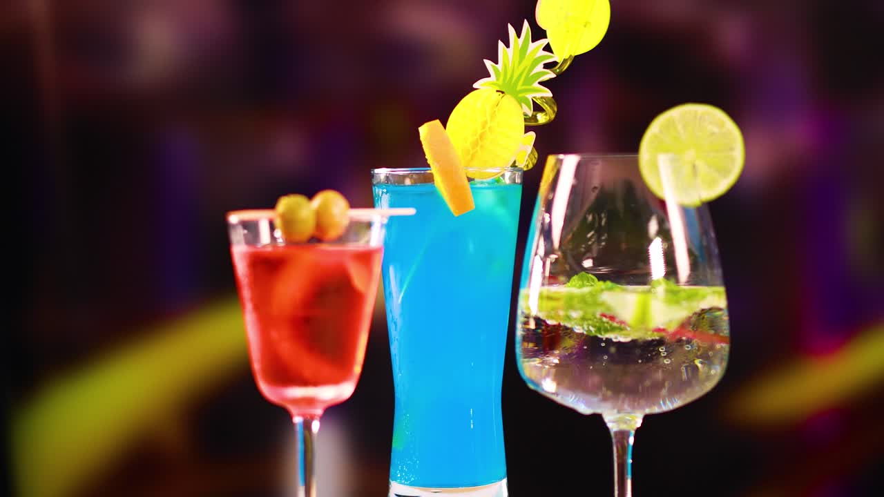 Three colorful cocktails with garnishes in a dimly lit bar, showcasing vibrant hues and dynamic composition