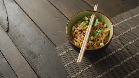 composition of bowl of pad thai with chopsticks on wooden background