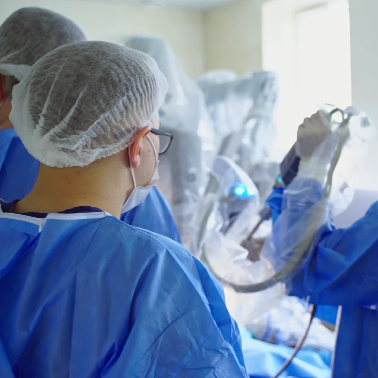 Medical specialists and surgical robot in operating rom. Doctors in medical uniform connect robotic arms for surgical procedure. Back view
