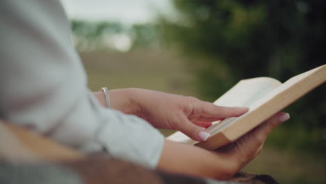 close-up side view of a woman holding a book on a blanket, with a softly blurred background featuring lush greenery, capturing a moment of tranquility