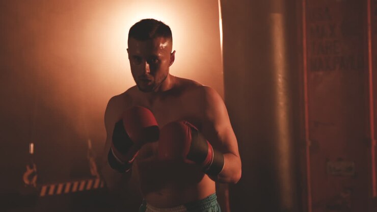 Boxeador sin camiseta mirando directamente a la cámara y haciendo movimientos de boxeo