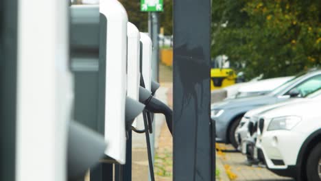 Sistema-De-Estación-De-Carga-De-Coches-Eléctricos-En-Una-Calle-De-La-Ciudad,-Un-Cable-Conectado-A-Un-Coche,-Futuro-Del-Automóvil,-Energía-Limpia-Y-Sostenible,-Día-Nublado,-Tiro-Medio-Desenfocado