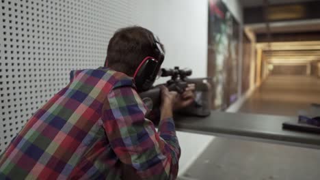 rara vista de un hombre disparando usar un rifle en el campo de tiro en auriculares