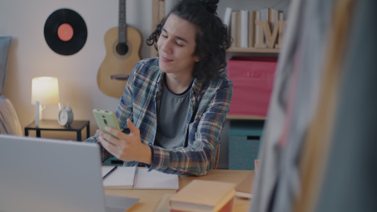 Teenage boy smiling while using his smartphone in his bedroom