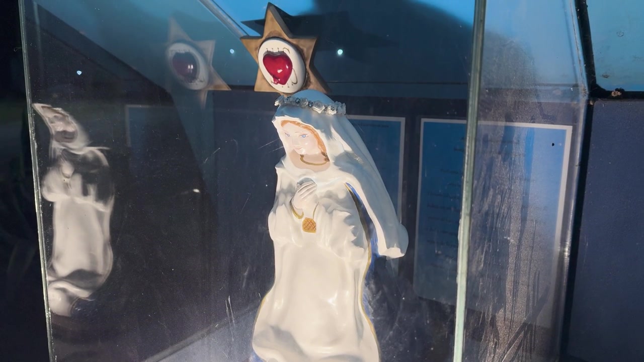 Nahaufnahme einer Marienstatue in einer Glasvitrine, beleuchtet von sanftem, fokussiertem Licht in einem katholischen Wallfahrtsort in Entre Ríos, Argentinien.