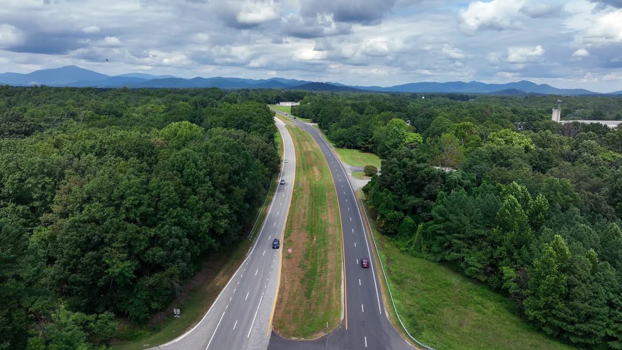 Traffic scene on American highway surrounded by forest trees and blue ridge mountains of Virginia in background. Cloudy summer day in America. Aerial Static wide shot