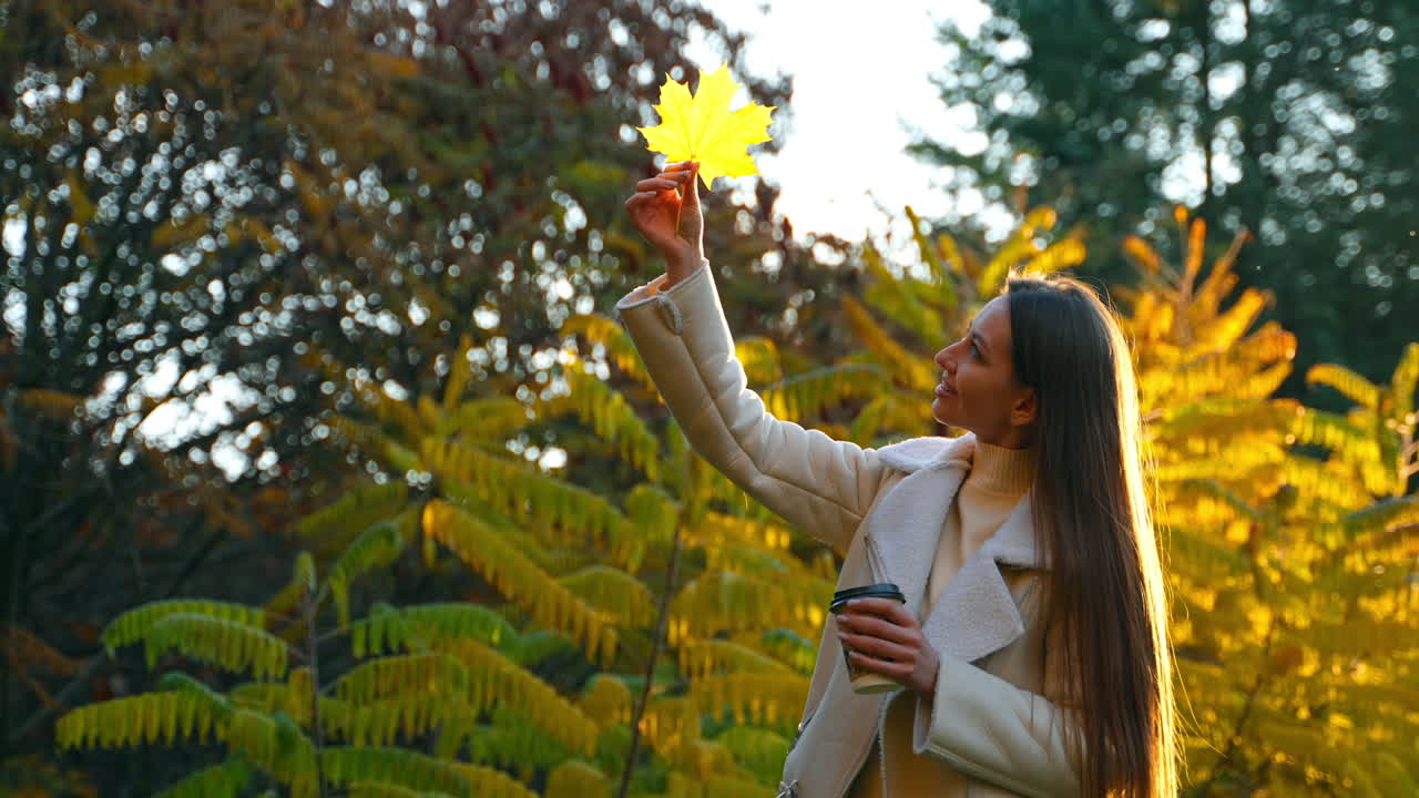 Woman enjoying autumn in a park with coffee and a leaf