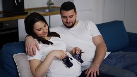 Portrait-of-pregnant-woman-and-her-husband-holding-baby-shoes-on-belly