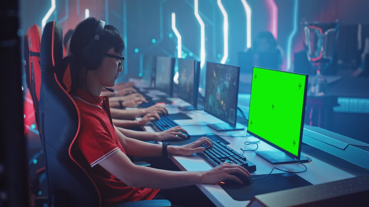 Professional Gamer Plays in a Video Game with Mock-up Green Screen Display on a Championship. Team of Pro Gamers in Stylish Neon Cyber Games Arena. Online Broadcasting of Tournament. Side View