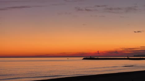 Small-boat-leaves-harbor-on-calm-sea-under-Orange-Dawn-skies