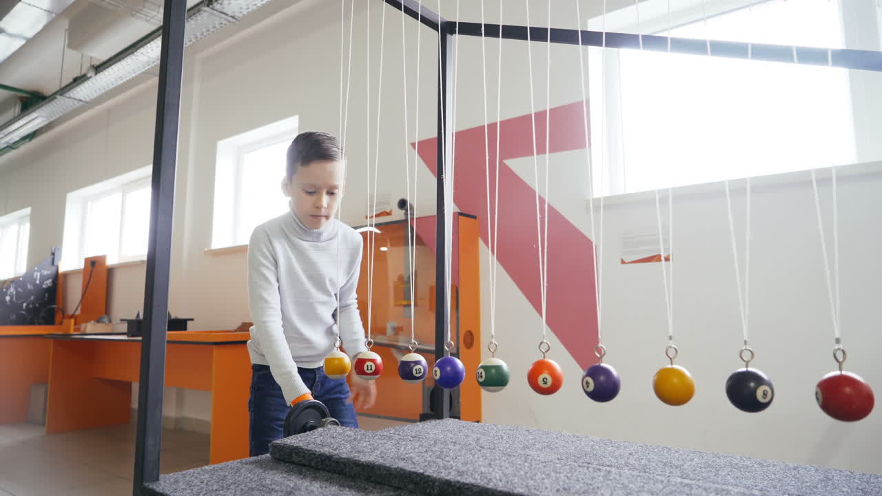 Boy makes an experiment with Newton's pendulum. The concept of physics. Museum of Science