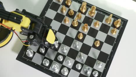 primer plano brazo robot amarillo jugando al ajedrez en el tablero de ajedrez