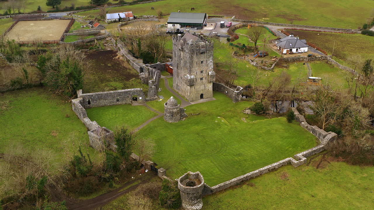 Aerial establishing orbit of Aughnanure Castle in Ireland, perched beside a winding river amid lush green fields