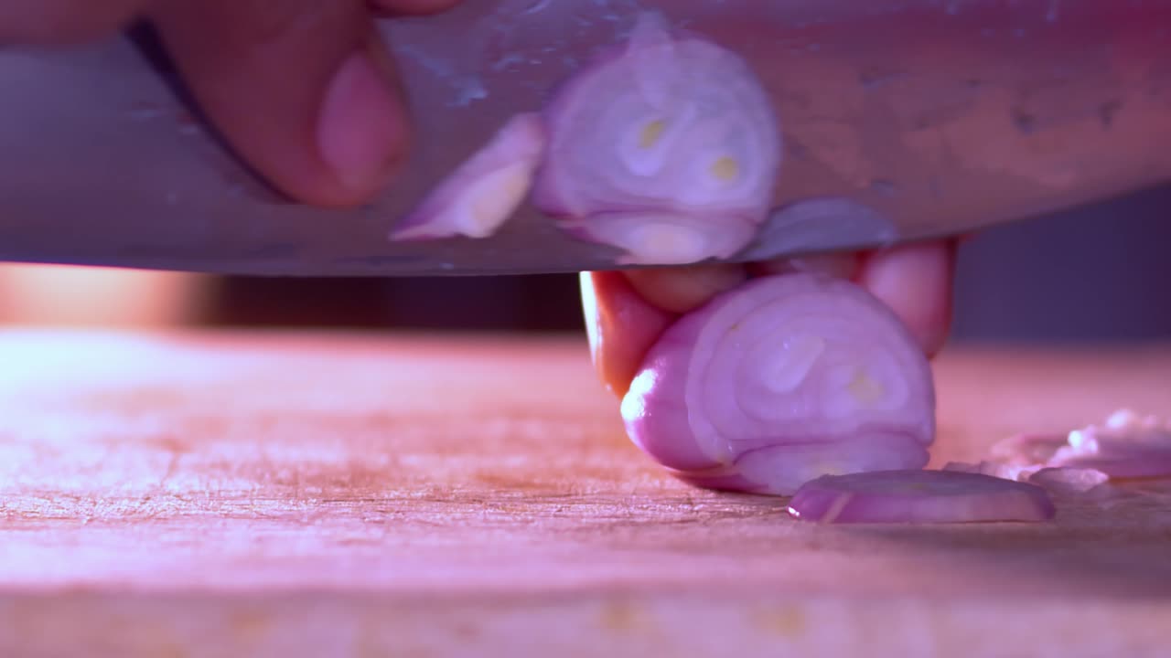 Close up video of the hands of a man cutting thin slices of onion on a wooden chopping board