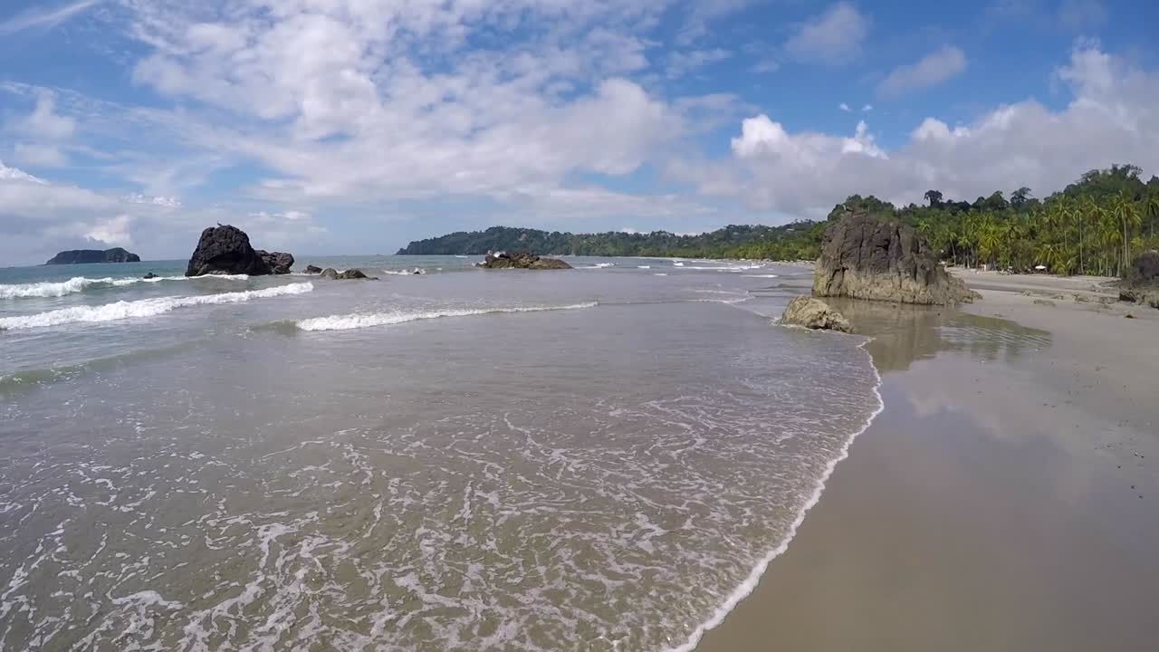 Pemandangan lebar sudut rendah di atas pantai Pasifik tropis dengan bebatuan, Pantai Manuel Antonio Kosta Rika, hari yang cerah, konsep perjalanan