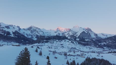 Aerial-view-capturing-the-tranquil-ambiance-of-sunrise-over-a-majestic-snowy-mountain-range-silhouette,-filmed-by-drone