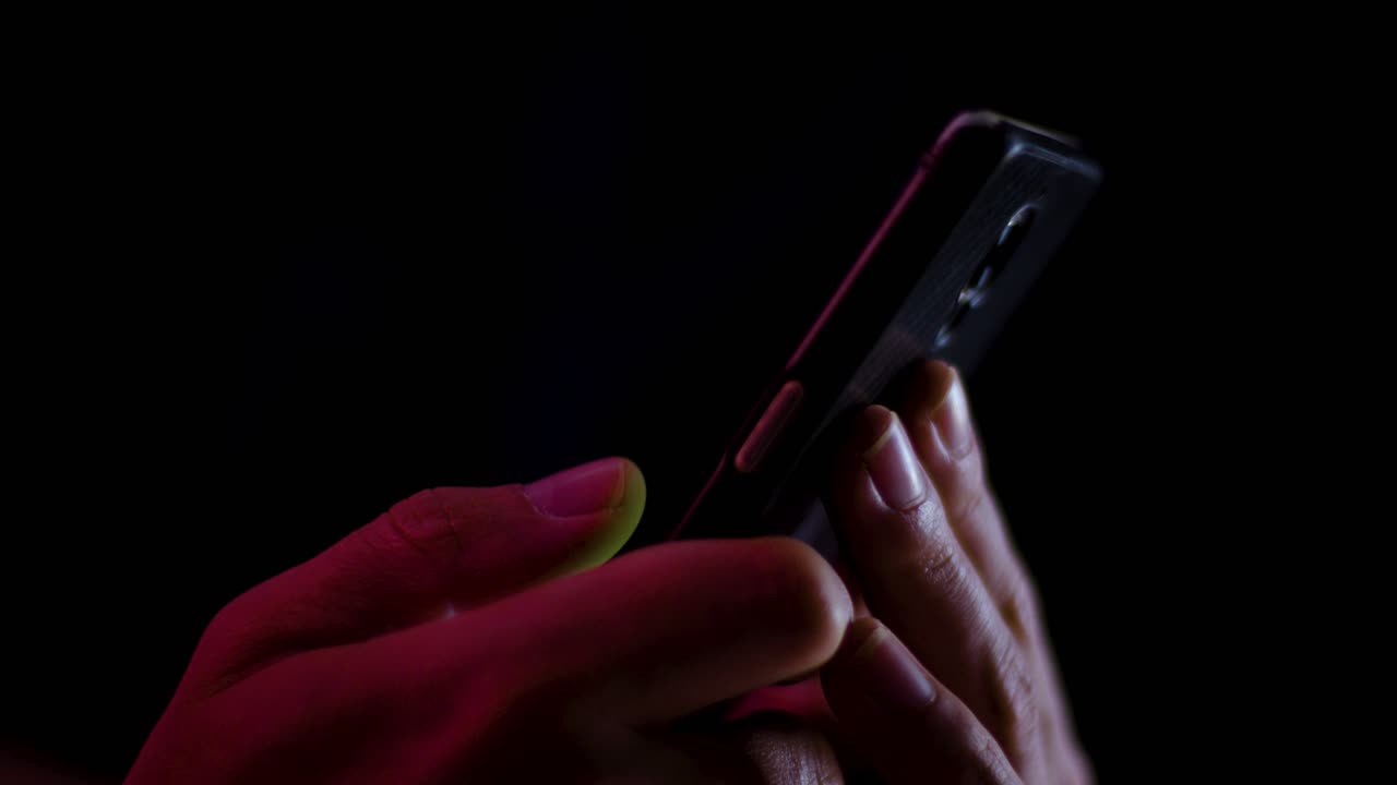 Thumb scrolling down and sideways on a smartphone close up in a dark room with red and white lightin