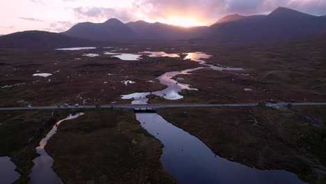 A-drone-slowly-flies-towards-a-bridge-crossing-a-wetland-landscape-of-islands-and-peat-bogs-surrounded-by-fresh-water-looking-towards-mountains-at-sunset