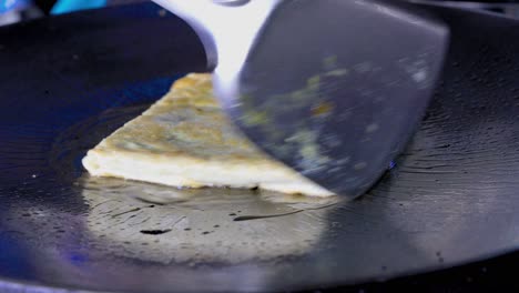 street food vendor is pan-frying and flipping murtabak, a spicy omelette pancake filled with bits of vegetables and minced meat, using a spatula and a fork