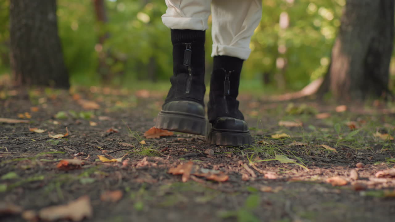 Leg view of happy walker strolling leisurely through forest path, black boots stepping on soft soil and fallen leaves, slow relaxed motion shot from low angle, suggesting calm outdoor exercise