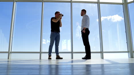 young businessman posing on camera indoors. professional photographer and a handsome man on big windows background. view from below.