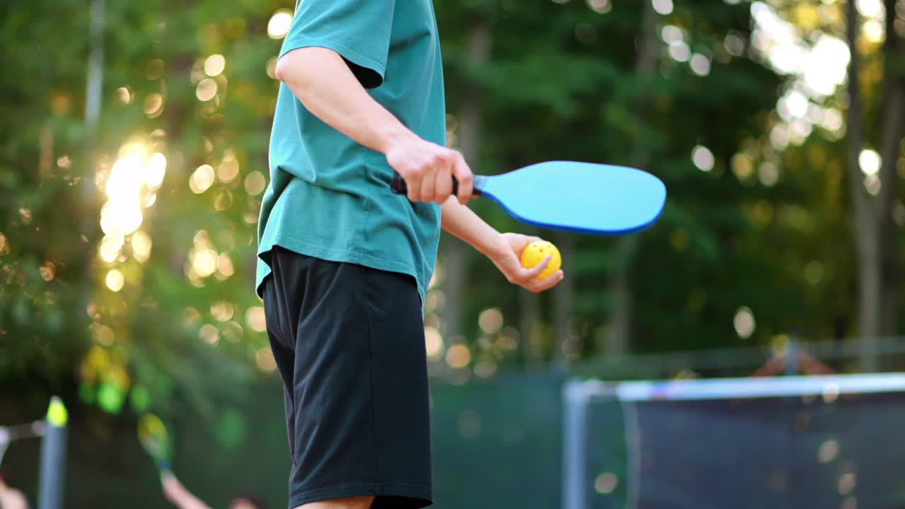 Man playing Pickleball, making ball pitch with a racket on an outdoor court. Slow motion