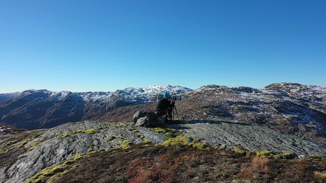 줌 렌즈와 삼각대가 있는 풍경 사진작가 주위를 천천히 돌고 있습니다 - 노르웨이 네스하임 산 엑싱게달렌의 아름다운 화창한 가을날 배경 시차 효과가 있는 산 꼭대기 클립