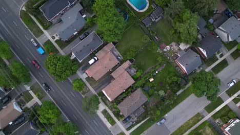 Top-down-aerial-of-cars-driving-along-streets-in-suburban-middle-class-neighbourhood-with-houses