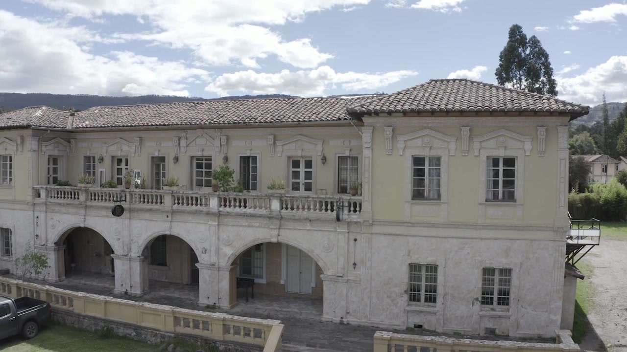 Ampia ripresa aerea con drone che mostra una pittoresca hacienda alla periferia di Quito, Ecuador. La vasta proprietà è circondata da una vegetazione lussureggiante, dolci colline e terreni agricoli tradizionali