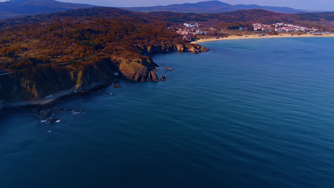 Allontanandosi dalla costa rocciosa con boschi in cima. Area residenziale sulla spiaggia sabbiosa sullo sfondo