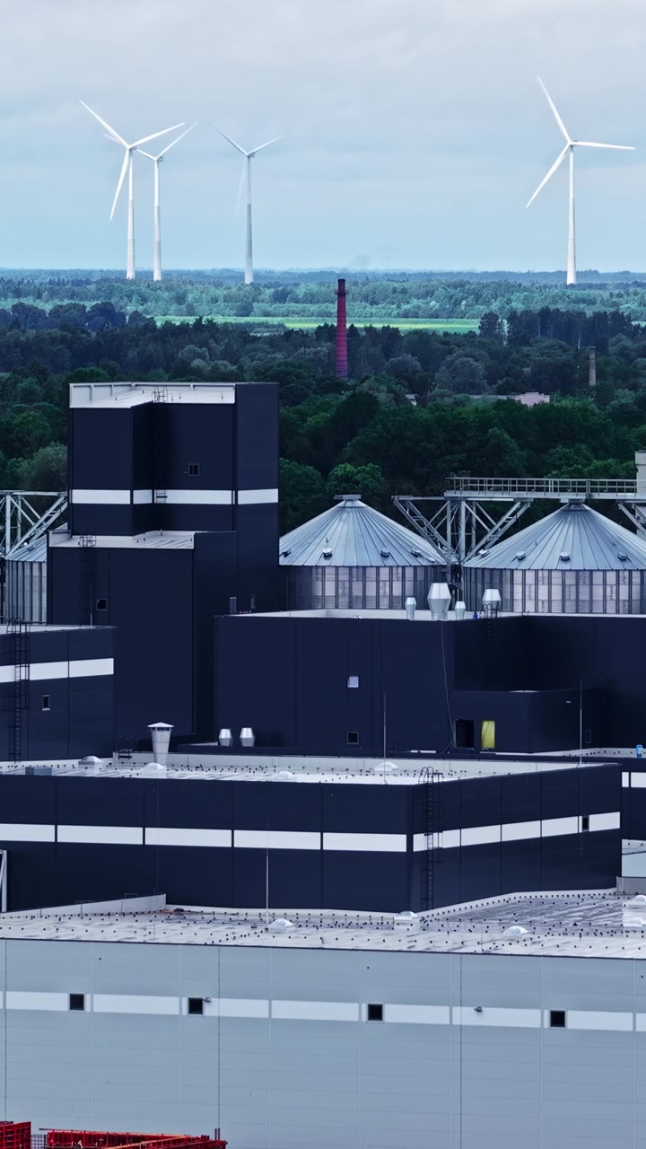 Data center facility with wind turbines generating renewable energy in background, aerial vertical static