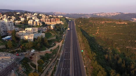 aerial view of an empty highway winding through a hilly landscape and residential area at dawn