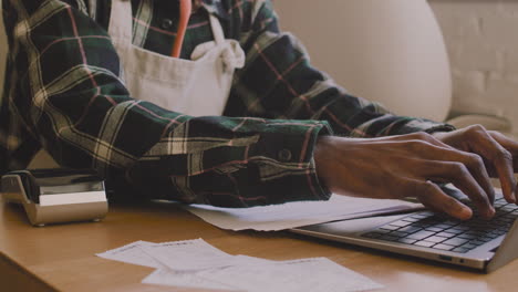 close up of an unrecognizable coffee shop owner sitting at table and calculating finance bill on laptop computer 2