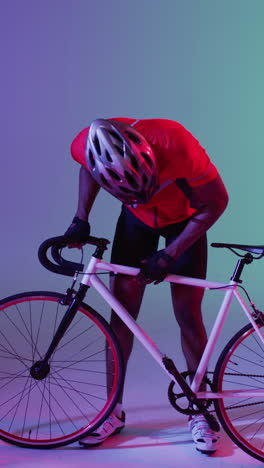 video vertical de un ciclista afroamericano con una bicicleta sobre una iluminación rosada