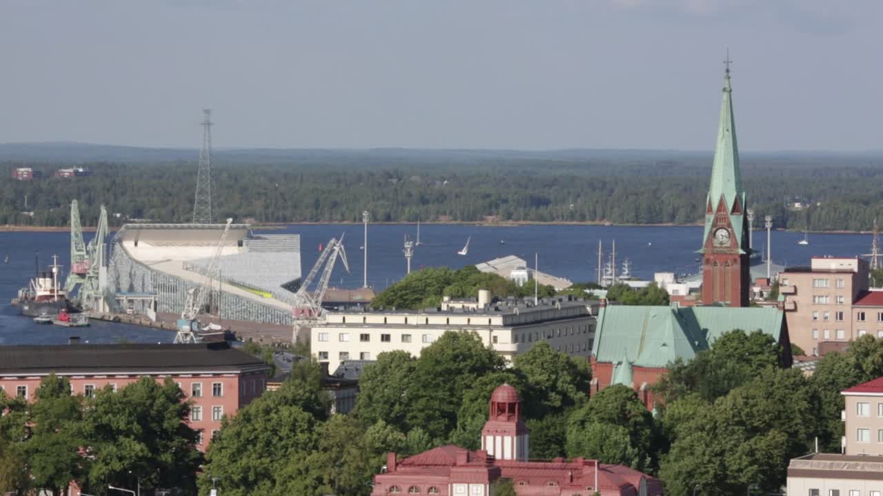 Veduta aerea con drone di Turku, Finlandia, con gru portuali, lungomare e la torre della Chiesa di San Michele che si erge sopra gli edifici della città sotto un cielo sereno.