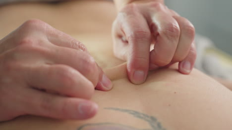 close up of female back with professional moving fingertips massaging muscles on massage bed under soft ambient lighting in spa environment offering soothing therapeutic care and physical relief