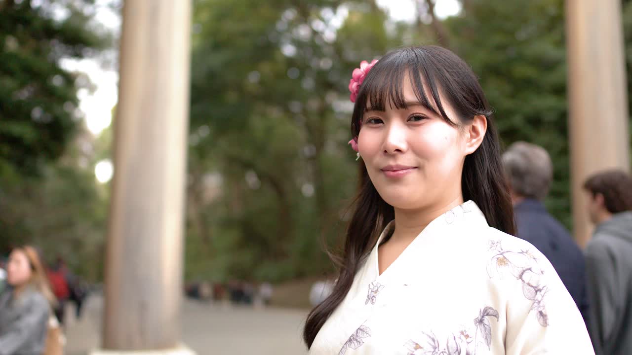 白い着物を着た若い女性が神社でカメラに向かって微笑んでいる。
