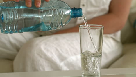 Young-woman-sitting-on-sofa-pouring-glass-of-water