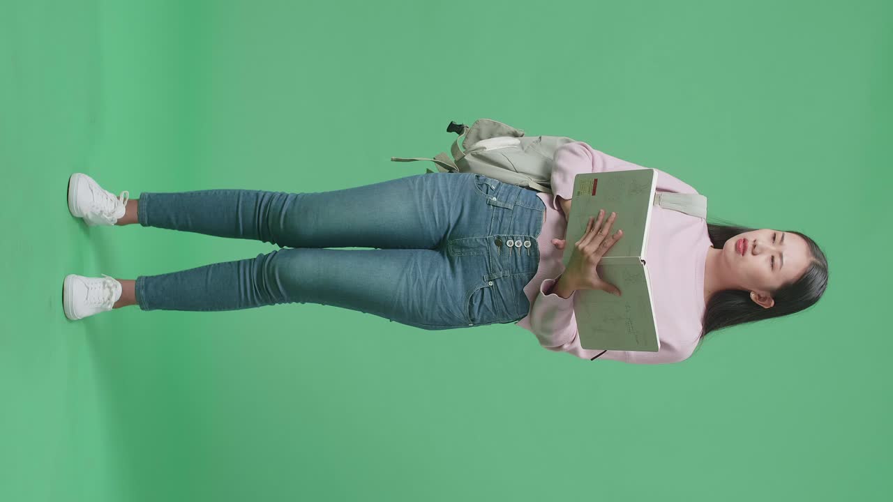 cuerpo lleno de estudiante asiática preocupada leyendo un libro en el estudio de pantalla verde