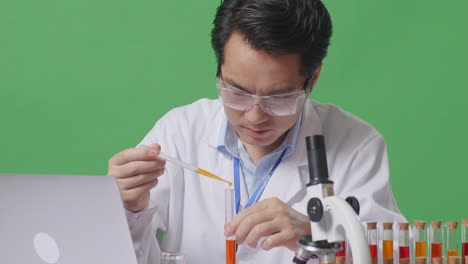close up of asian man scientist making experiment with test tube and screaming goal celebrating typing on a laptop on the table with microscope in the green screen background laboratory