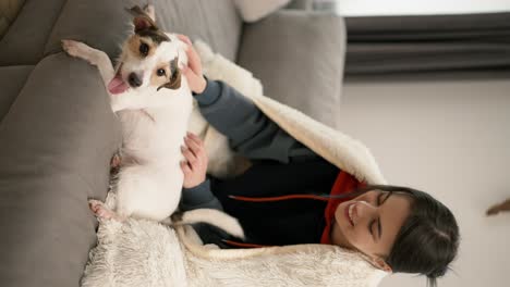 beautiful woman sitting on couch in blanket with her small dog jack russell terrier