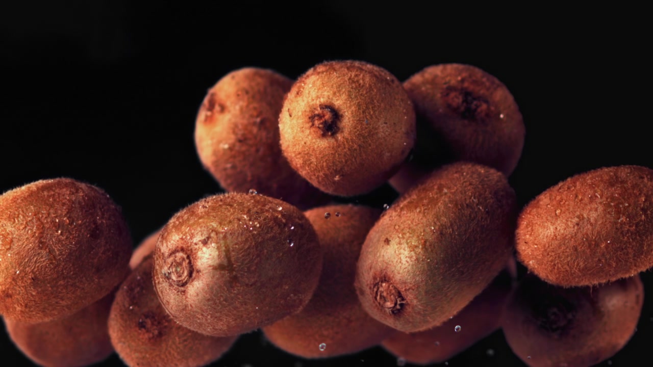 Kiwi freschi che galleggiano verso l'alto con goccioline d'acqua su sfondo nero
