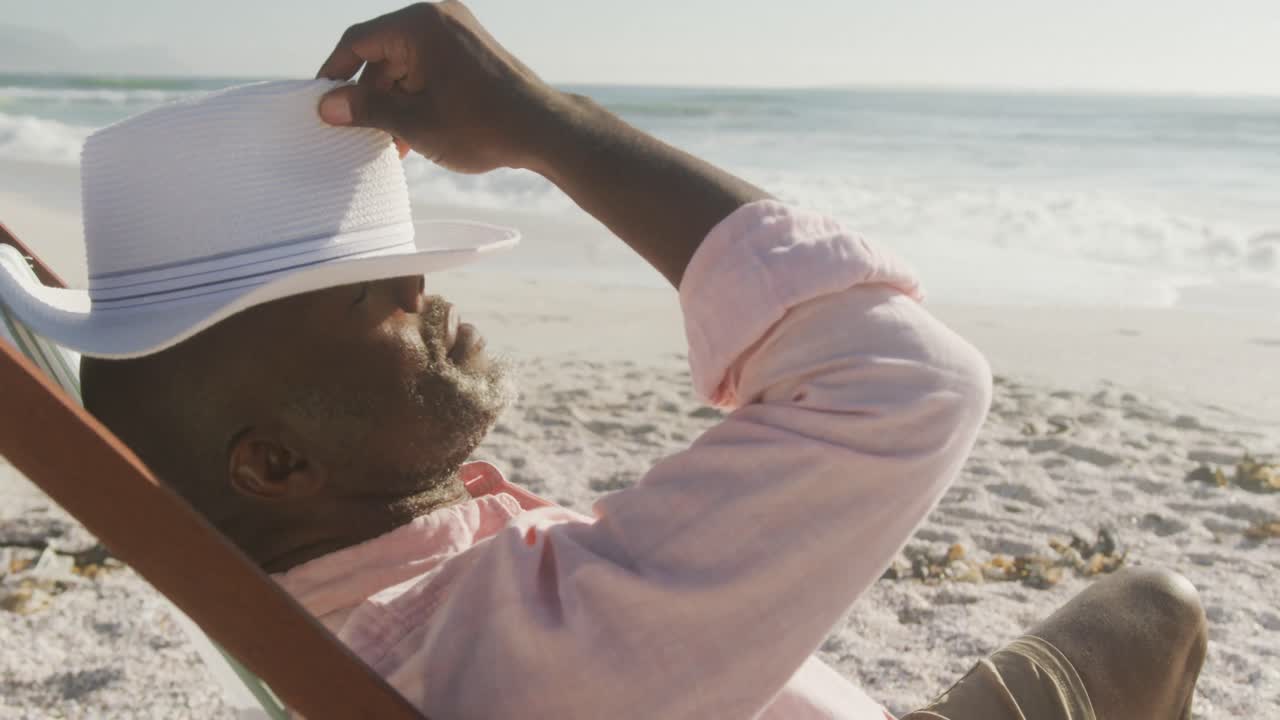 Ældre afroamerikansk mand ligger på liggestol på solrig strand