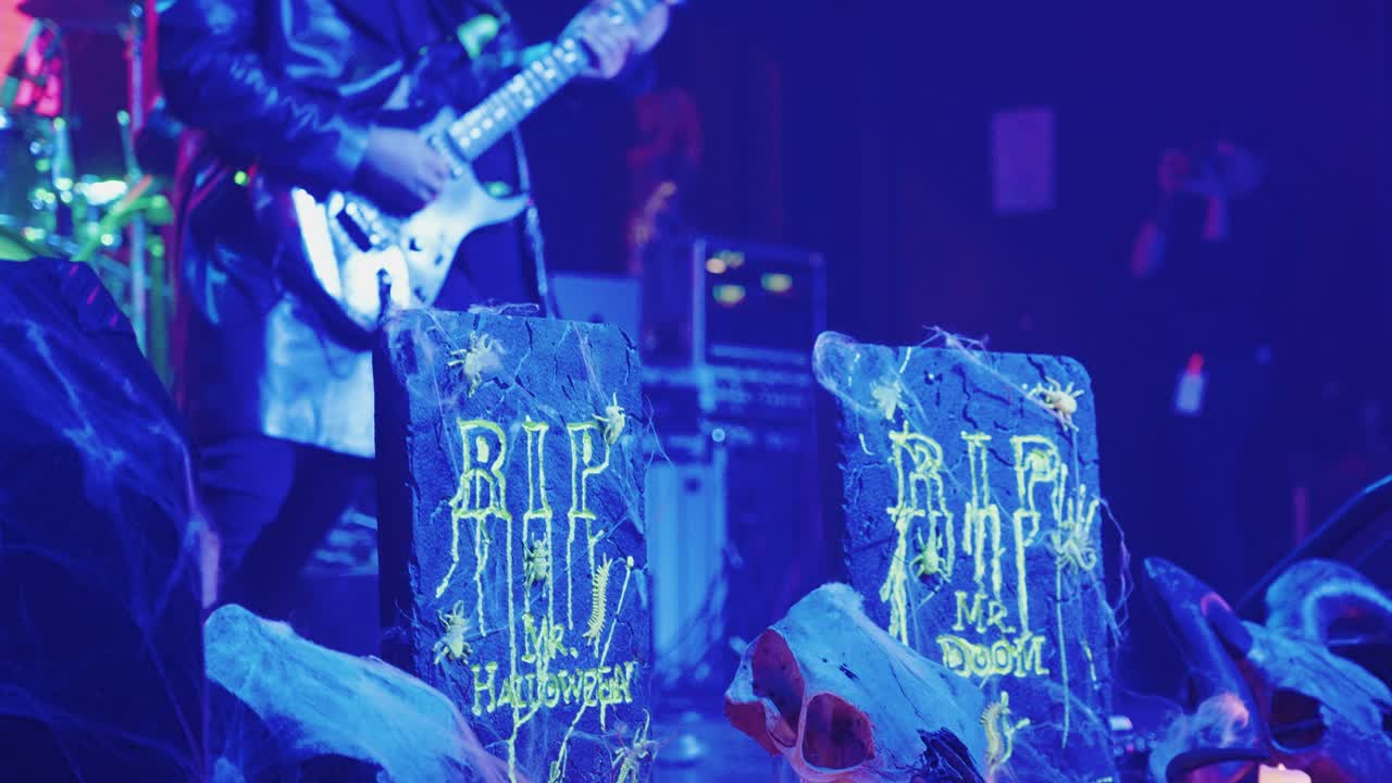Gitarrist spelar på en scen med Halloween-tema och blå belysning.