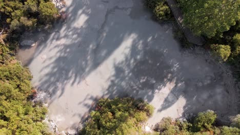 ascending aerial top view of steam rising from hot bubbling mud pools within a forest at golden hour