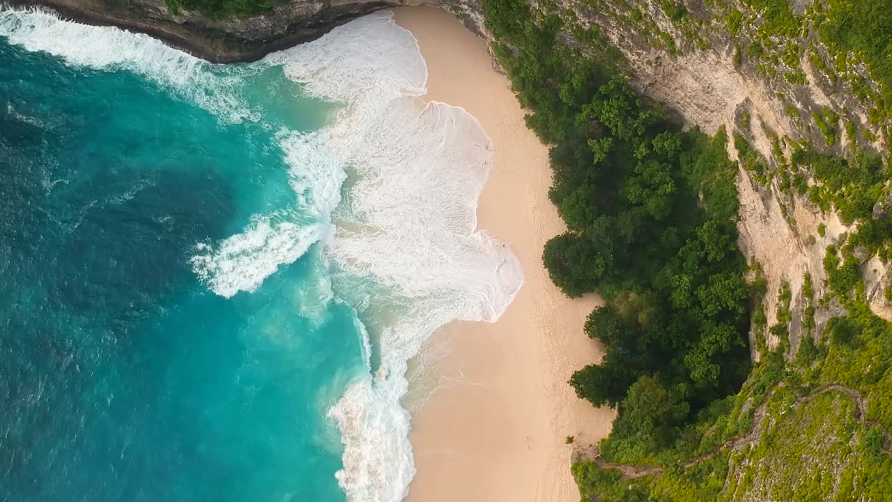 Ripresa aerea con drone della spiaggia di Kelingking con bellissime onde blu che si infrangono sulla riva in Indonesia.
