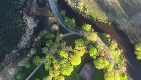 Top-view-of-cars-driving-along-rural-road,-by-lake-and-meander-winding-river-in-early-morning