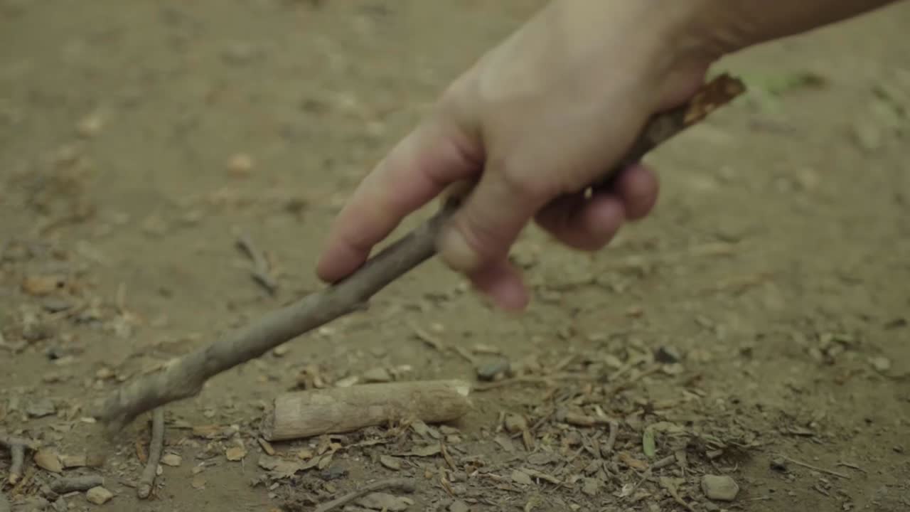 Hand with stick doodling in the dirt close up shot