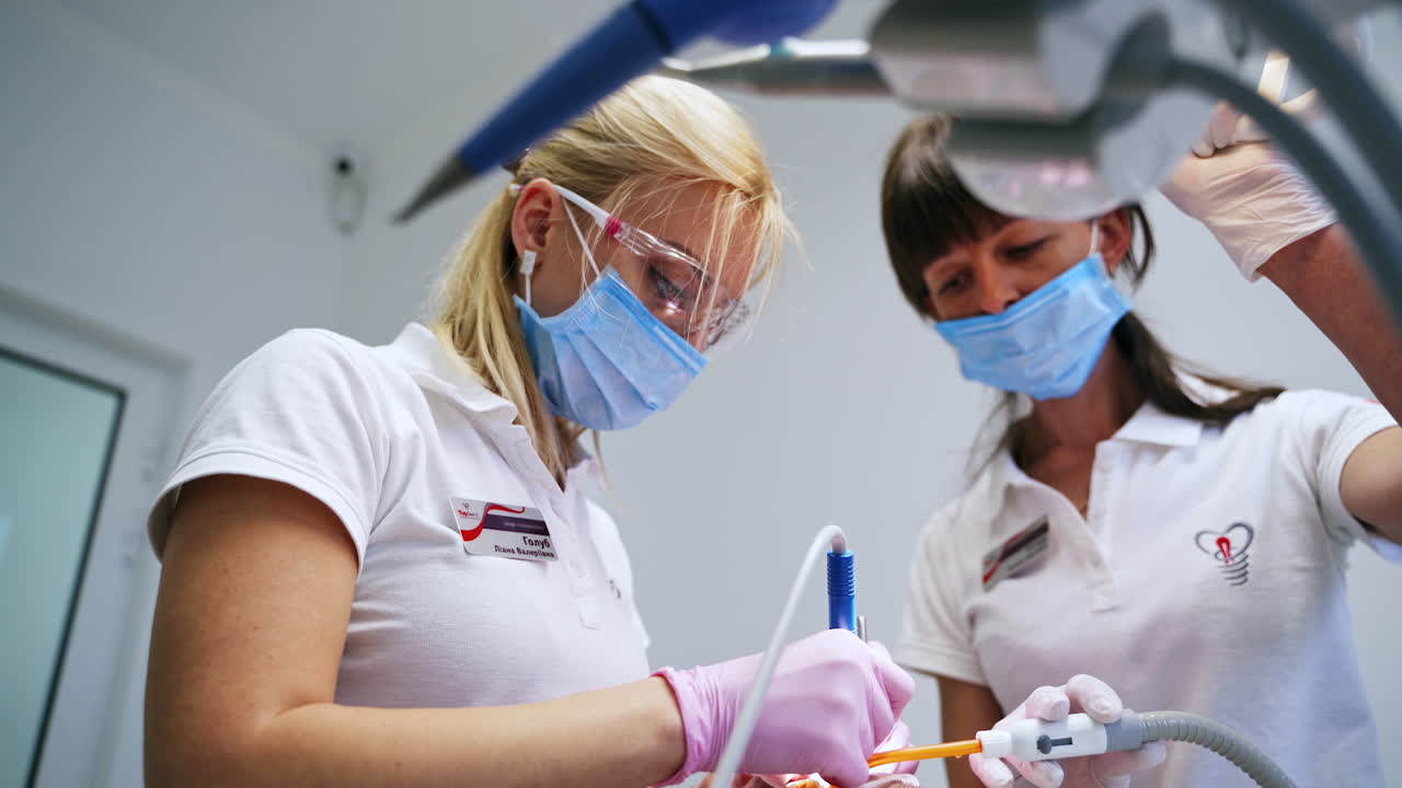 Female dentist using modern device instruments. Assisting nurse fixing the lamp over the patient. Low angle view.